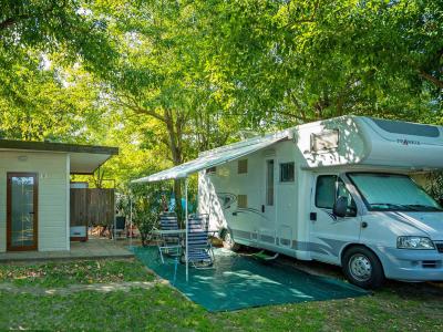 Camper geparkeerd naast een klein huisje in een schaduwrijk groen gebied.