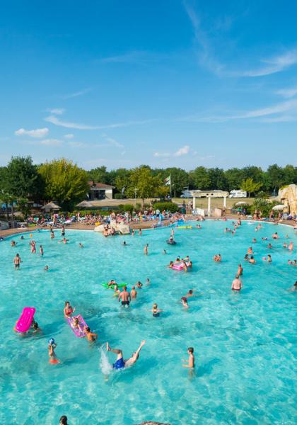 Crowded pool on a sunny day, surrounded by trees.