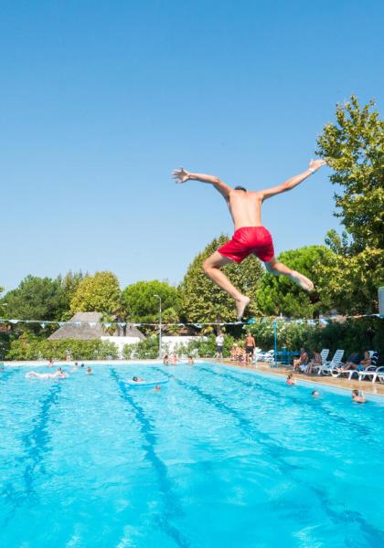 Ragazzo salta in piscina, giornata soleggiata.