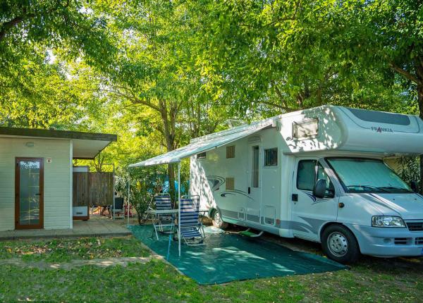 Camper geparkeerd naast een klein huisje in een schaduwrijk groen gebied.